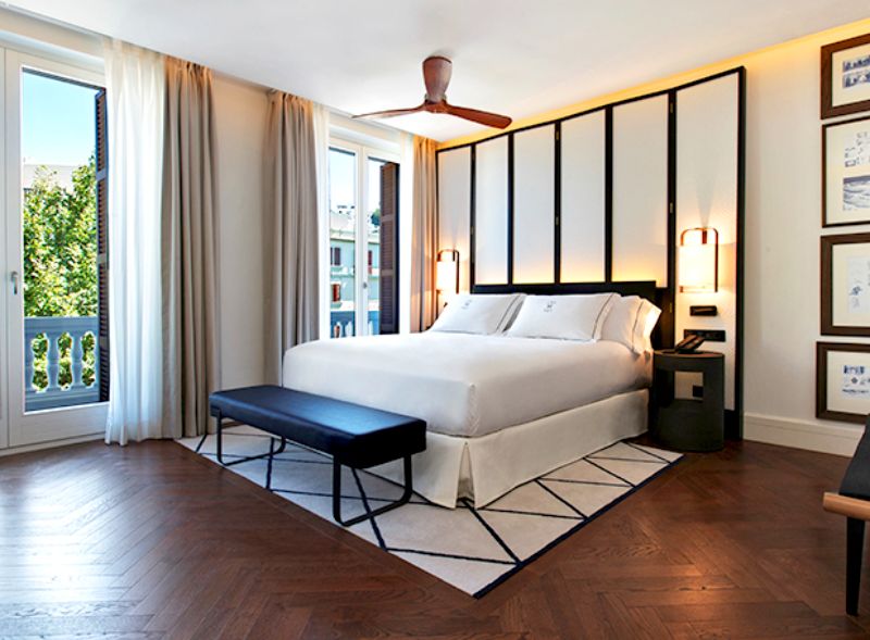 hotel bedroom with white bed, black and white geometric rug, black bench
