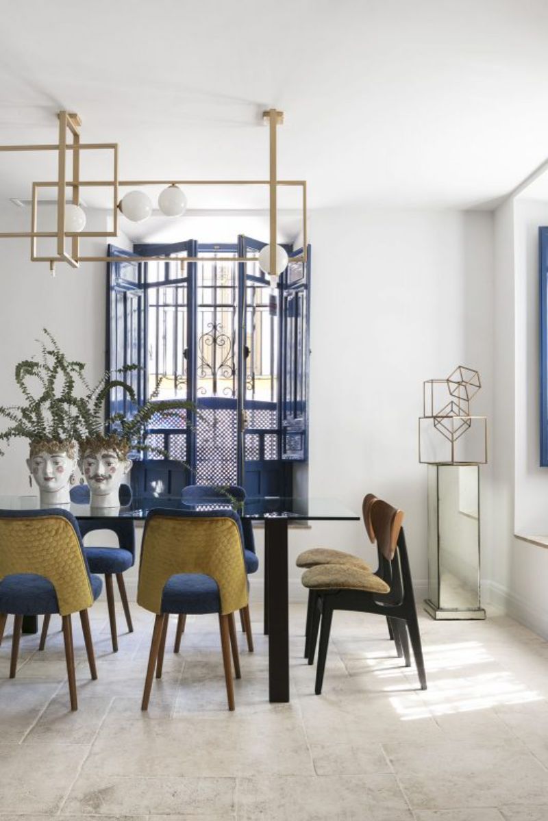 geometric suspension lamp, decorative elements, plants, blue dining chairs, glass dining table