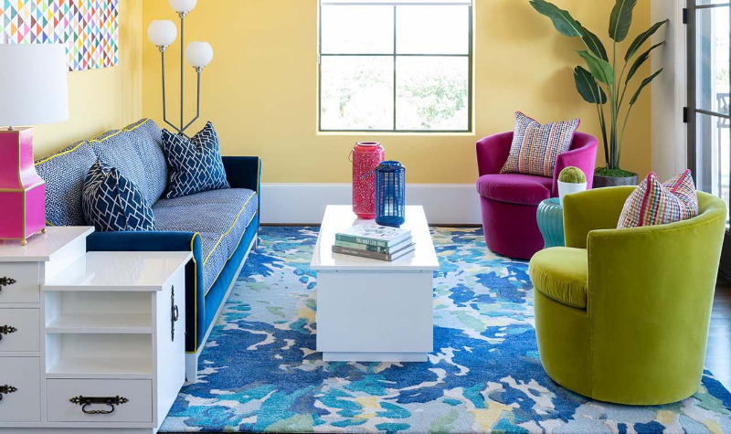 Rug Design Ideas From Pamela Hope Designs. A colorful living room, there's a multi-colored rug with a blue sofa and a pink and a yellow single sofa.
